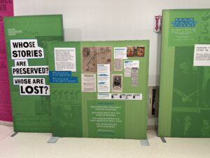 Two green exhibition graphic panels, with the title "Whose stories are preserved? Whose are lost?"