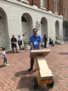 A man wheeling a prototype museum exhibition kiosk on a sidewalk.