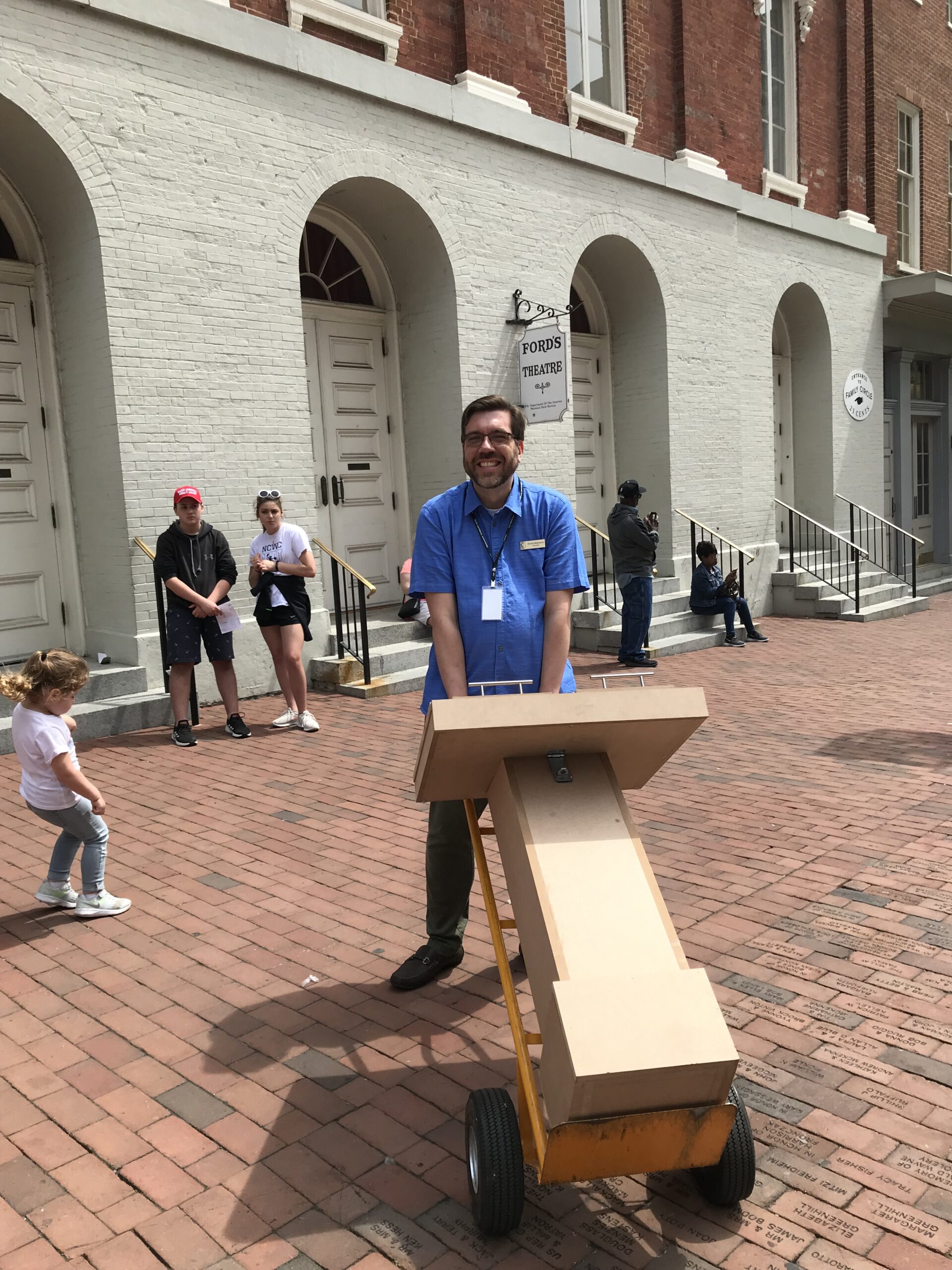 A man wheeling a prototype museum exhibition kiosk on a sidewalk.