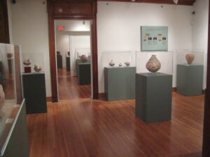 A room with elaborately painted clay pots in cases and graphics on the wall.