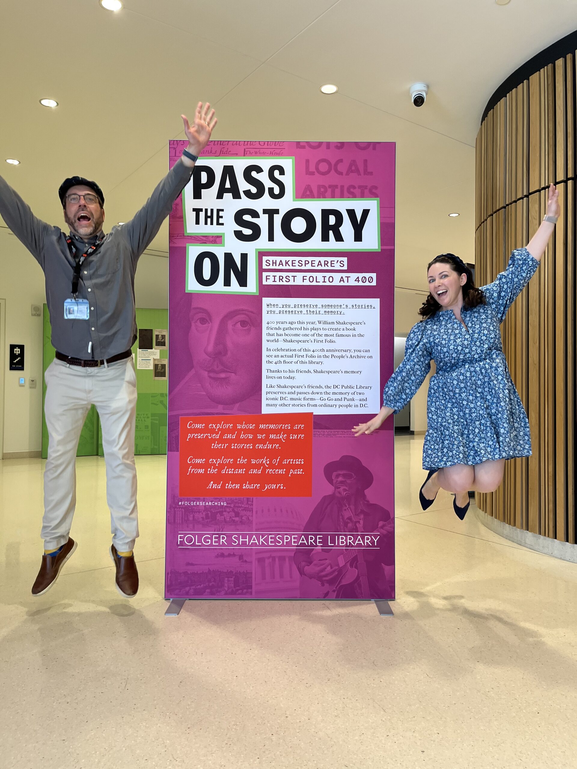 Two people jumping with joy at the introductory graphic panel for an exhibition called "Pass the Story On: Shakespeare's First Folio at 400."