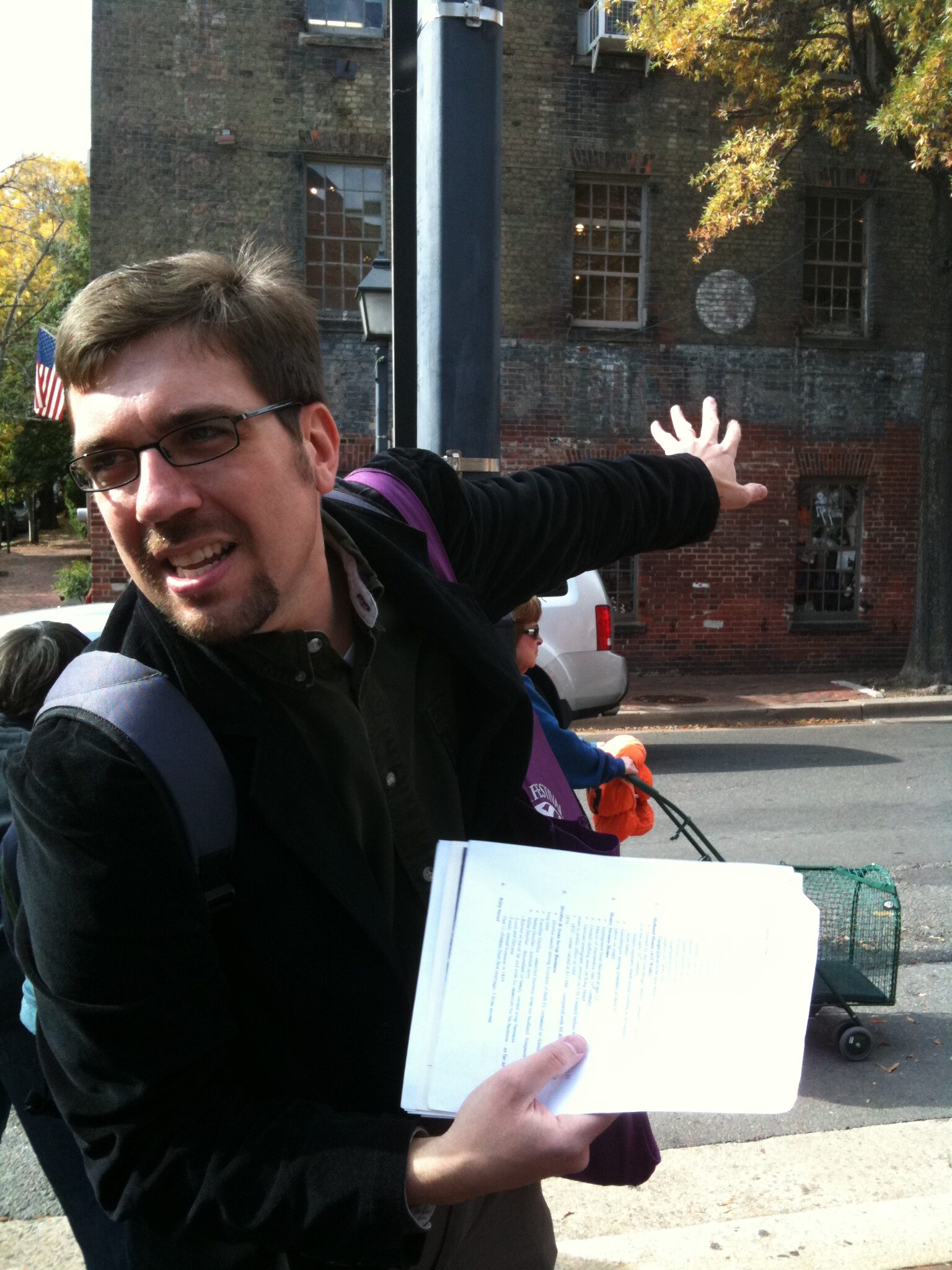 A man leading a walking tour, gesturing to a historic brick building.