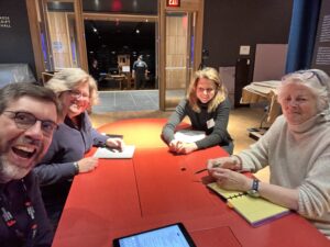 A group of four people meeting at a red table in a museum gallery.