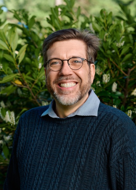 A man smiling in front of a batch of green.