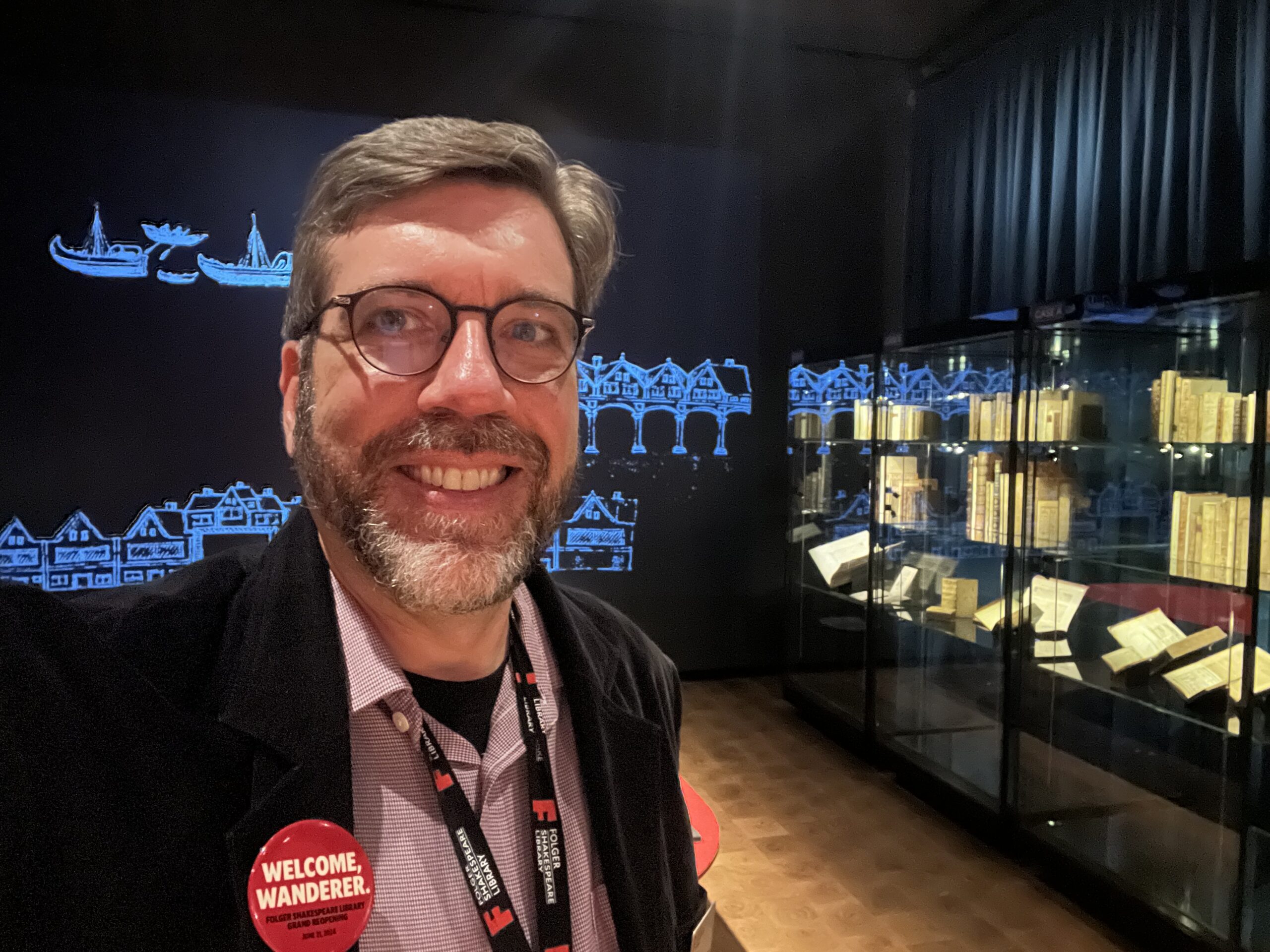 A man smiling in front of an exhibition case filled with books.