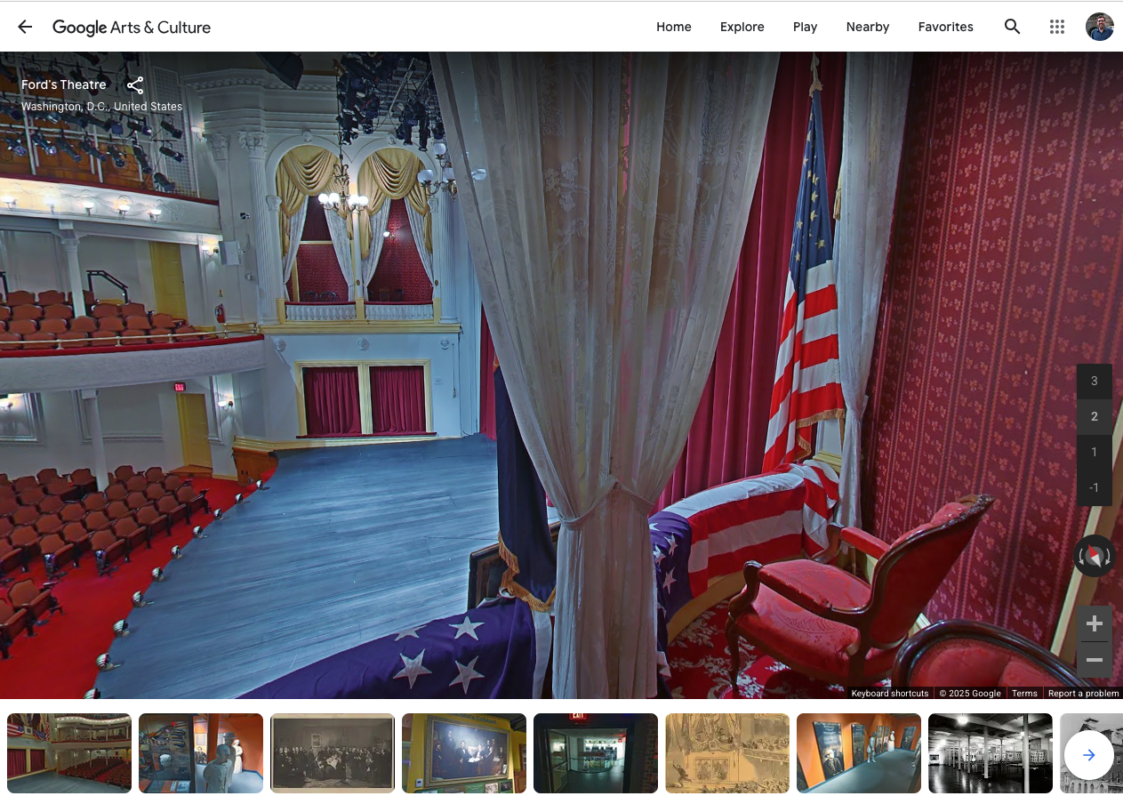 A view onto a stage in a recreated theater from the 1800s, including a U.S. flag to the right and fancy Victorian furniture and curtains.
