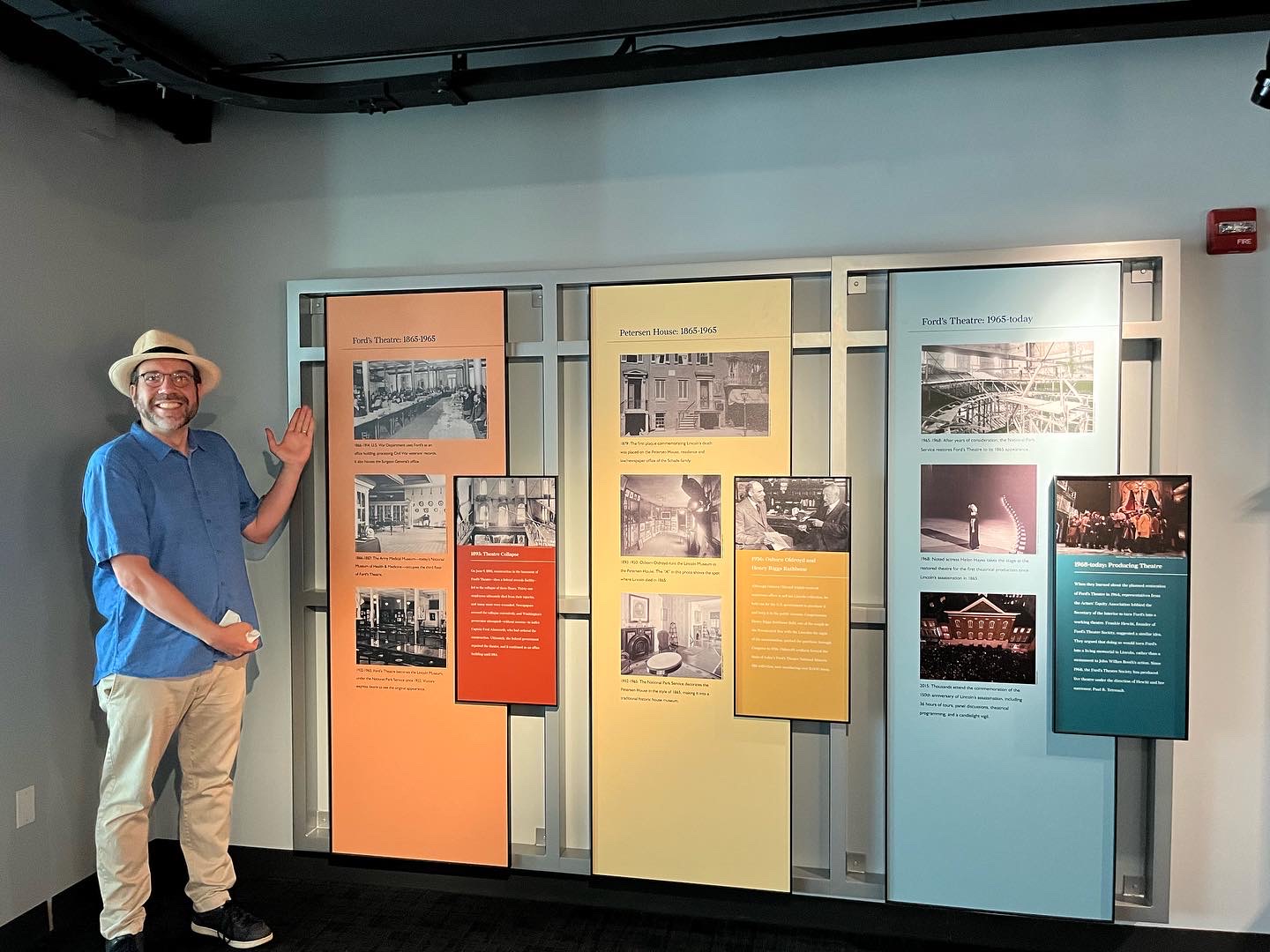 A man standing in front of 3 large graphic panels, each containing four historic images plus text.