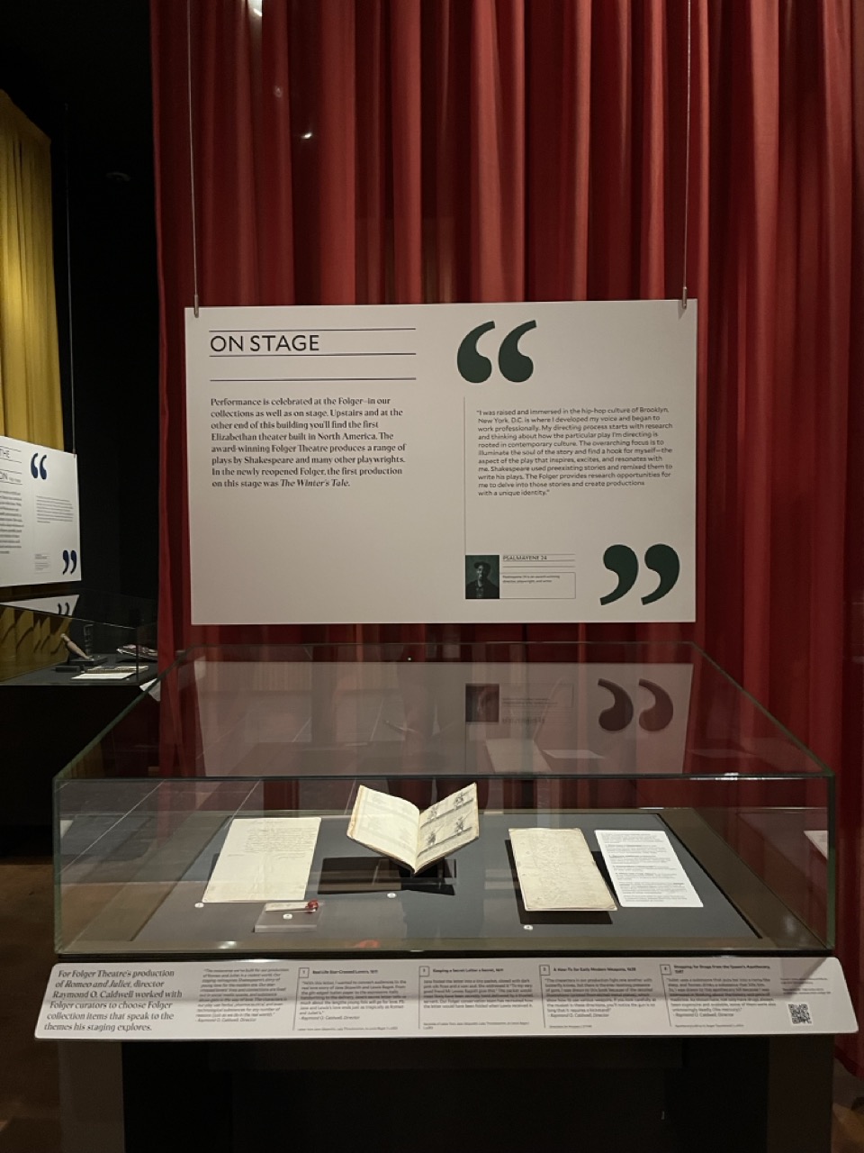 A museum exhibition case showing books and manuscripts, with a sign above it that says "On Stage."